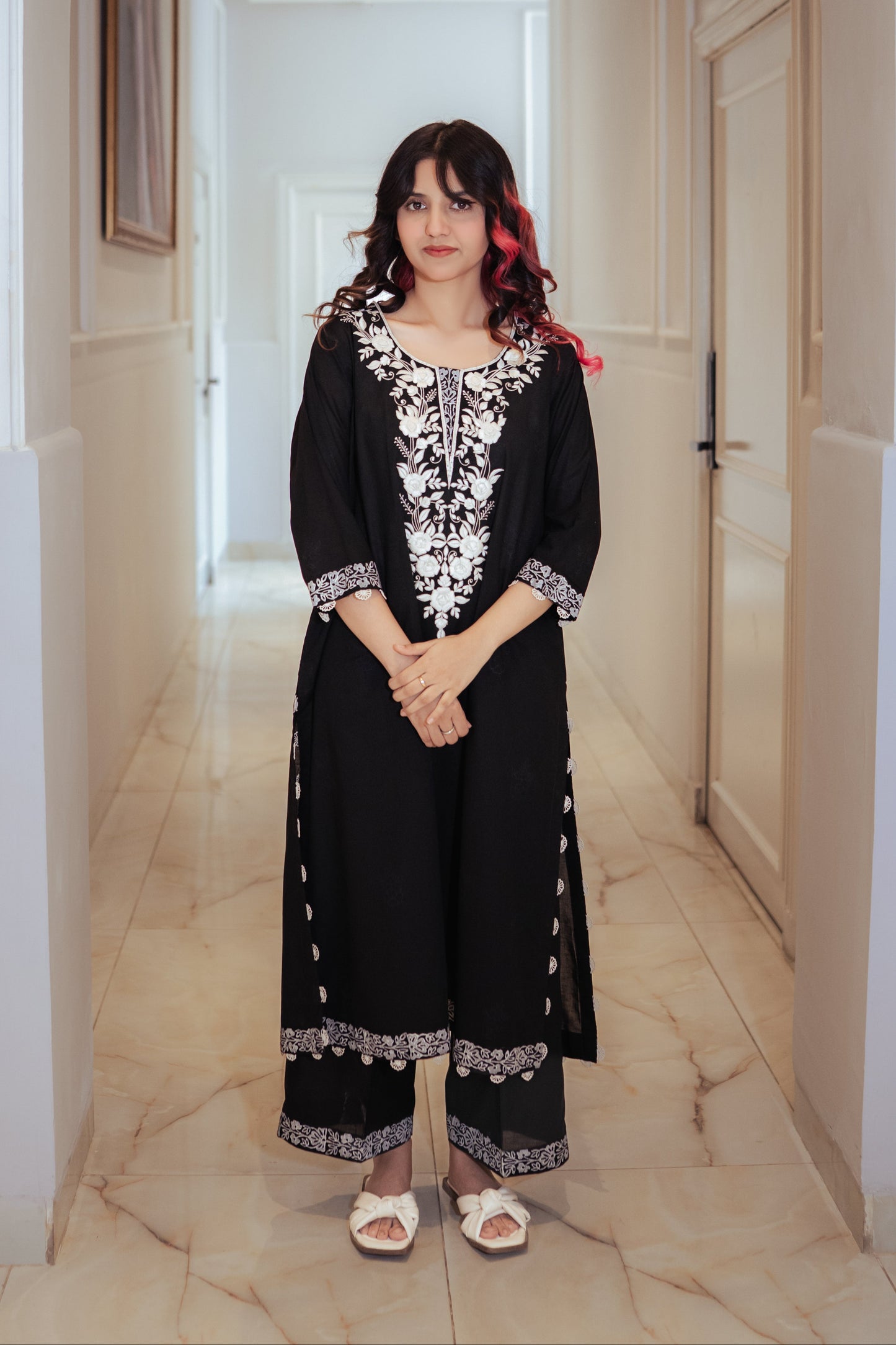 Woman in a black outfit with white patterns standing in a hallway.