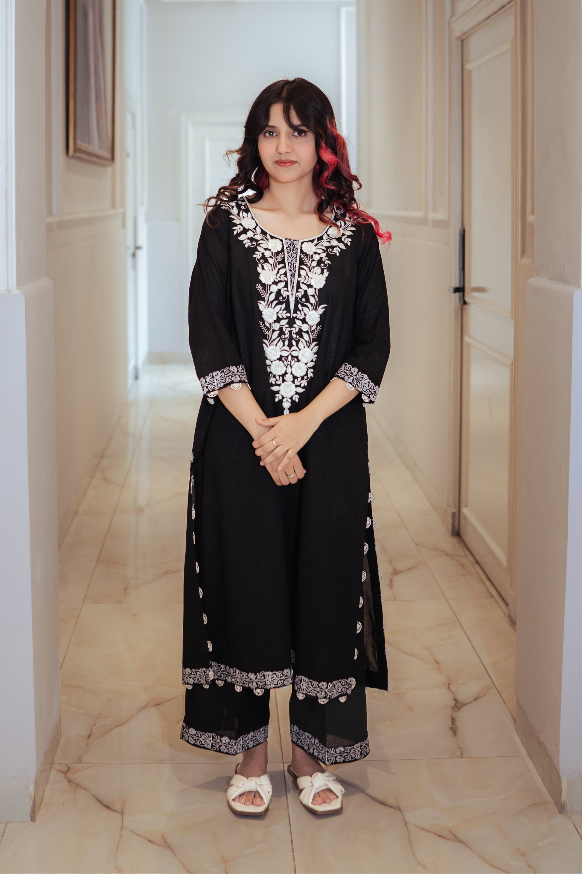 Woman in a black outfit with white patterns standing in a hallway.